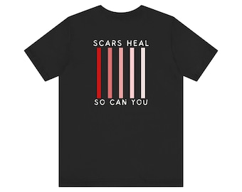 Può includere: Maglietta nera con il testo "SCARS HEAL SO CAN YOU" in bianco. Ci sono sei strisce verticali rosse, rosa e bianche dietro il testo.