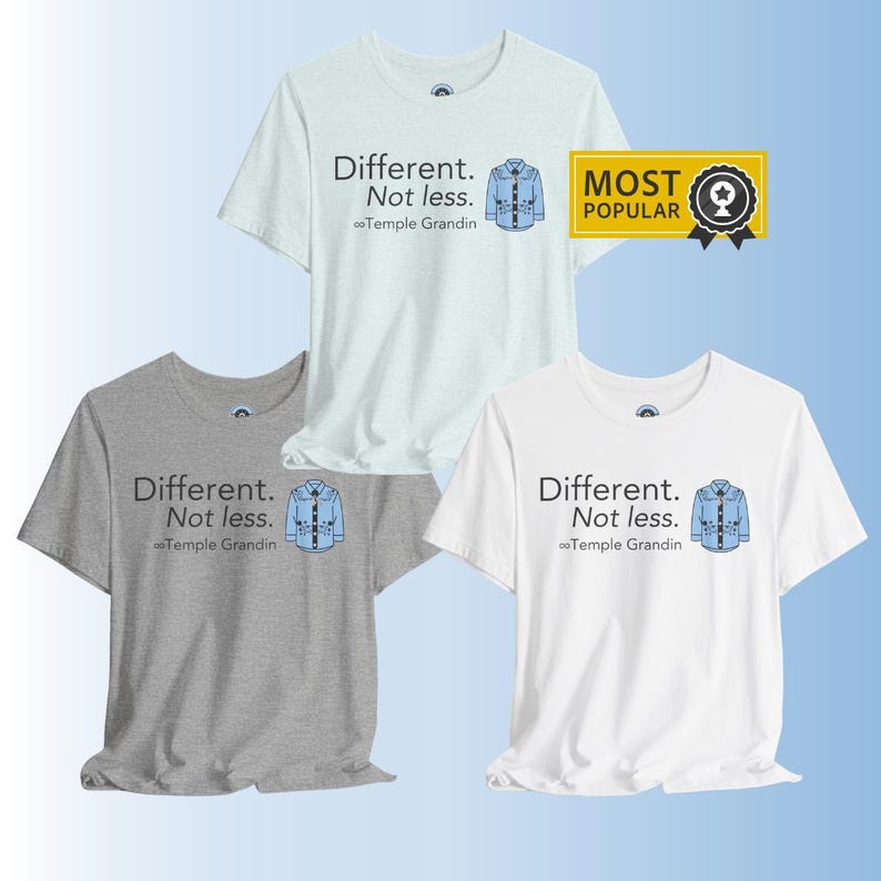 Pu&ograve; includere: Tre t-shirt a maniche corte con girocollo in azzurro, grigio melange e bianco. Ogni maglietta presenta il testo "Different. Not less." sopra il nome "Temple Grandin" e una piccola grafica di una camicia blu con un simbolo di infinito.