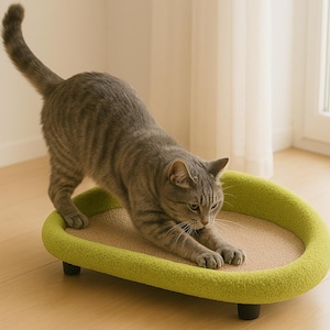 May include: A grey tabby cat stretches on a green oval-shaped cat bed with a sisal scratching surface.