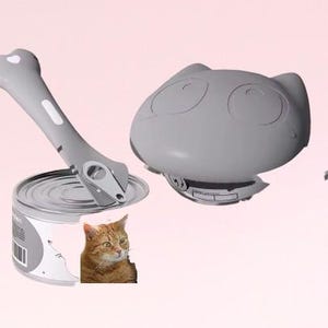 K&ouml;nnte beinhalten: Ein grauer, katzenf&ouml;rmiger Dosen&ouml;ffner mit einem wei&szlig;en Griff. Der Dosen&ouml;ffner ist ge&ouml;ffnet und liegt auf einer Dose Katzenfutter. Eine Katze schaut in die Kamera.