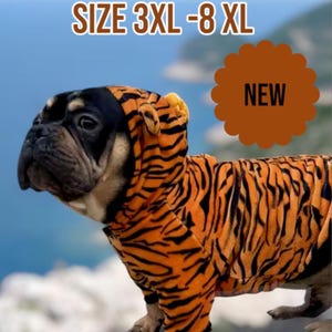 May include: A small, brown and black dog wearing a tiger-striped hooded sweater. The sweater has black stripes on an orange background. The dog is looking to the left of the image. The text "SIZE 3XL-8XL" is at the top of the image. The text "NEW" is in a brown circle at the top right of the image.
