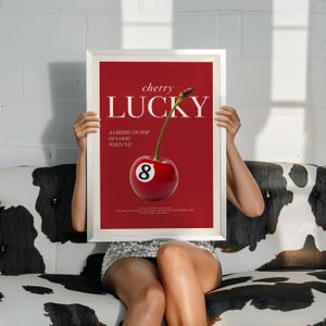 K&ouml;nnte beinhalten: Ein rotes und wei&szlig;es Poster mit dem Text "cherry lucky" und einer Kirsche mit einer Acht-Ball-Kugel darauf. Der Text unter der Kirsche lautet "A cherry on top of good fortune!"