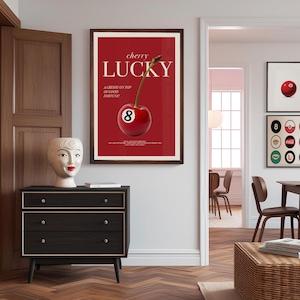 K&ouml;nnte beinhalten: Ein rotes und wei&szlig;es Poster mit dem Text "cherry lucky" und einer Kirsche mit der Nummer 8 darauf. Das Poster ist in braunem Holz gerahmt und h&auml;ngt an einer wei&szlig;en Wand.