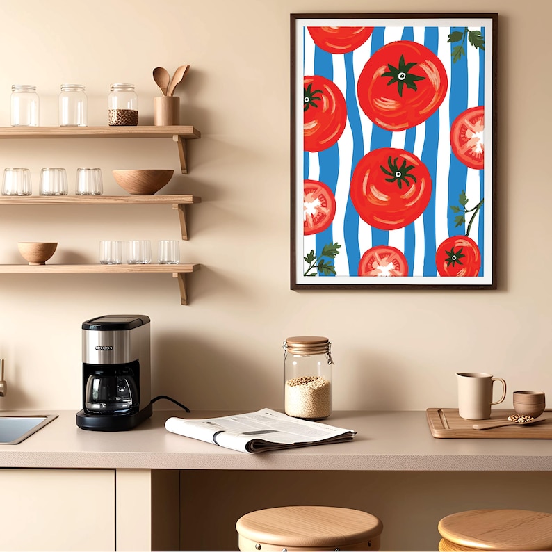 May include: A framed print of red tomatoes on a blue and white striped background. The tomatoes are arranged in a random pattern and some are cut in half. The print is hanging on a light beige wall above a kitchen counter.