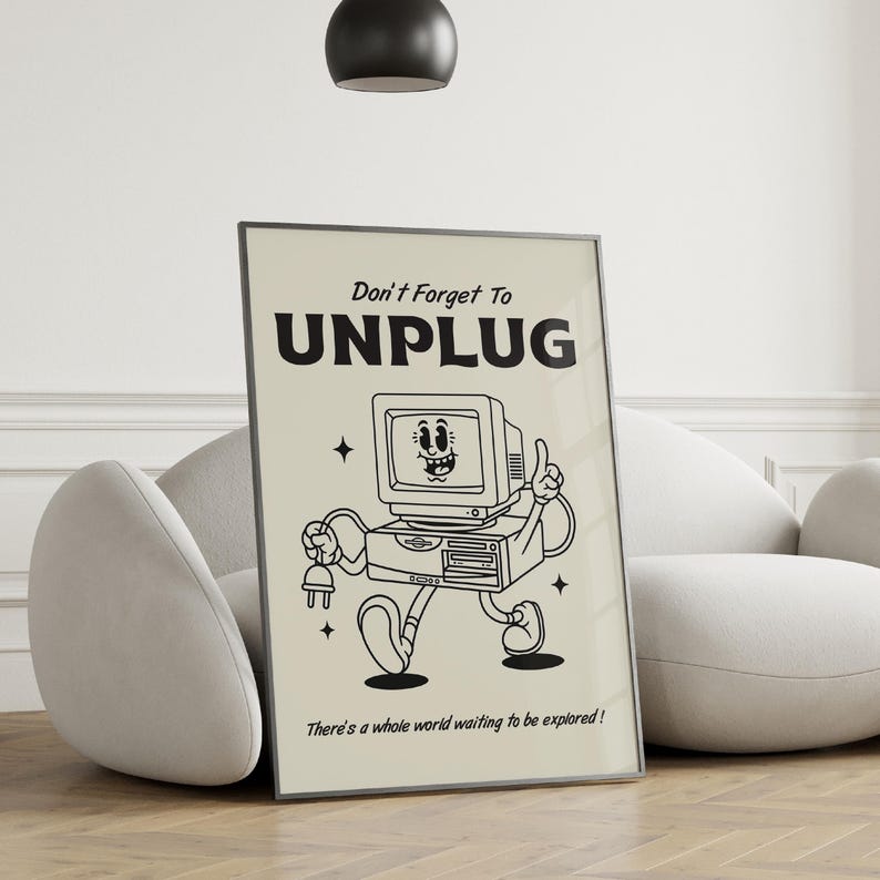 Op de afbeelding: Een ingelijste poster met een retro cartoon computerpersonage, die een stekker vasthoudt en loopt. De poster heeft de tekst "Don't Forget To UNPLUG" en "There's a whole world waiting to be explored!" in zwart op een cr&egrave;mekleurige achtergrond.
