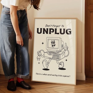 Op de afbeelding: Een ingelijste poster met een retro cartoon computer illustratie. De poster leest "Don't Forget To UNPLUG" boven de computer graphic, en "There's a whole world waiting to be explored!" eronder. De lijst is licht van kleur.