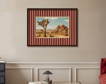 May include: Framed art print featuring a desert landscape with a Joshua tree and rock formations under a blue sky. The artwork is framed with a dark brown border and a red and pink striped pattern.