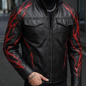 Könnte beinhalten: Schwarze Lederjacke mit roten Flammenmustern auf den Ärmeln. Die Jacke hat einen Reißverschluss, zwei Brusttaschen und einen Stehkragen. Ein stilvolles Oberbekleidungsstück.