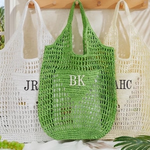 May include: Three crocheted tote bags in white, green, and cream. Each bag has a rectangular pocket with initials embroidered on the front. The white bag has "JR", the green bag has "BK", and the cream bag has "AHC".