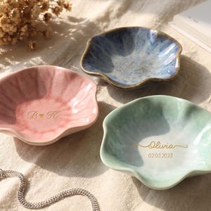 Pu&ograve; includere: Tre piatti in ceramica con bordi smerlati, rosa, blu e verde. Il piatto rosa ha "B & K" e un cuore. Il piatto blu ha un nome, e il piatto verde ha un nome e una data. Una catena d'argento &egrave; in primo piano.