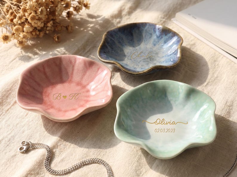 Pu&ograve; includere: Tre piatti in ceramica con bordi smerlati, rosa, blu e verde. Il piatto rosa ha "B & K" e un cuore. Il piatto blu ha un nome, e il piatto verde ha un nome e una data. Una catena d'argento &egrave; in primo piano.