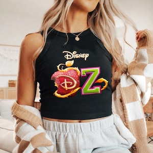 May include: Black tank top featuring the Disney logo and a graphic of a red apple with the letter "Z" in green and pink. The apple has a bite taken out of it, and the Disney logo is in gold.
