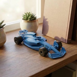 May include: A blue toy race car with black wheels sits on a wooden shelf. The car is a detailed model of a Formula 1 vehicle. A small succulent plant in a beige pot is nearby.