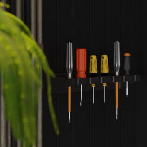 May include: A black wall-mounted tool organizer holding various screwdrivers. The screwdrivers have orange, yellow, and silver handles. The image is set against a black background with a hint of a green plant in the foreground.