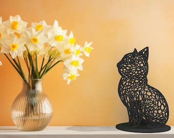 Puede incluir: Un jarrón de cristal transparente con estrías verticales contiene un ramo de narcisos blancos con centros amarillos. A la derecha, una escultura de gato calada negra. El fondo es un degradado de naranja y amarillo.