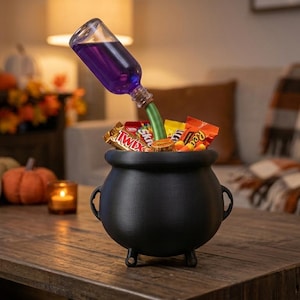 May include: A black cauldron with three small feet, filled with various candy bars. A clear glass bottle containing purple liquid is tilted at an angle, with its neck extending into the cauldron, creating a floating potion effect.