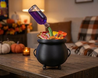 May include: A black cauldron with three small feet, filled with various candy bars. A clear glass bottle containing purple liquid is tilted at an angle, with its neck extending into the cauldron, creating a floating potion effect.