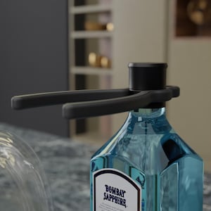 Può includere: Un versatore per bottiglie nero con un design a leva è attaccato a una bottiglia di gin Bombay Sapphire. La bottiglia di gin è trasparente, di colore azzurro chiaro, con un'etichetta bianca e blu navy. Il versatore ha una parte superiore cilindrica e due bracci orizzontali.