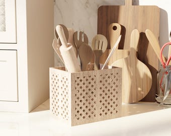 May include: A wooden kitchen utensil holder with a geometric pattern, filled with various wooden cooking tools, including a rolling pin, spoons, and forks. Several wooden cutting boards are in the background, creating a rustic kitchen theme.