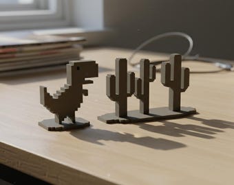 May include: A gray, pixelated dinosaur figurine and a set of three pixelated cactus figurines sit on a light-colored wooden surface. The figurines are in a minimalist, retro style, reminiscent of early video game graphics.