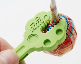 May include: A light green plastic tool with a serrated circular opening designed to assist in opening a wrapped lollipop. The tool features the embossed text Chupa and includes two additional circular indentations on its flat handle surface.