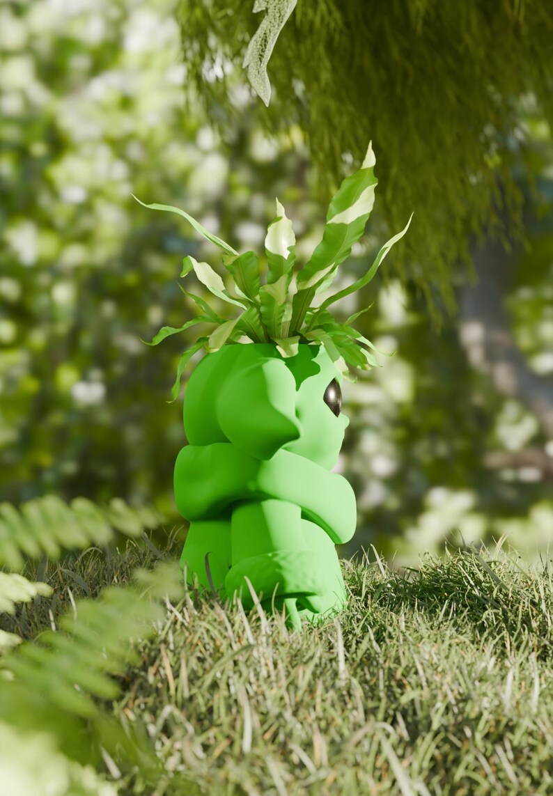 May include: A vibrant green, stylized planter shaped like a character, holding a plant with green and white leaves. The planter has a smooth, rounded design and a single eye. The image is set outdoors in a grassy area with a blurred background of green foliage.