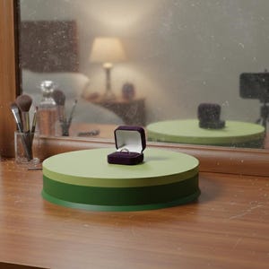 May include: A ring in a purple velvet box sits on a two-toned green and light green platform. The platform is on a wooden surface, with a mirror reflecting the scene. Other items include perfume, makeup brushes, and a lamp.