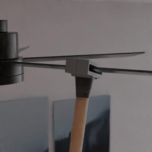 Puede incluir: Primer plano de un ventilador de techo moderno con aspas de color gris oscuro y un mango de madera clara. La carcasa del motor del ventilador es de color gris oscuro. Las aspas son finas y rectangulares, y el ventilador está montado en un techo blanco.