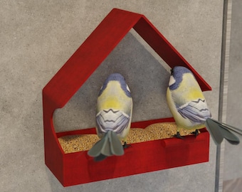 May include: A red bird feeder with a house-like roof, filled with seeds, and two small birds perched inside. The birds have blue, yellow, and gray feathers. The feeder is mounted on a gray wall.
