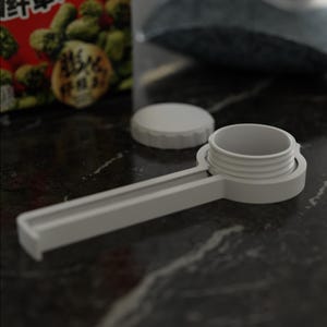 May include: A white plastic bag clip with a round cap and a long handle. The clip is designed to seal bags and containers. The clip is on a dark, textured surface.