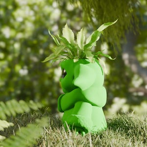 May include: A green ceramic planter shaped like a hugging figure, with a plant sprouting from the top. The planter is set in a grassy area with a blurred green background, suggesting an outdoor setting.