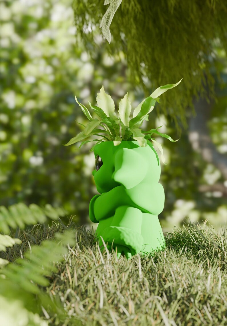May include: A green ceramic planter shaped like a hugging figure, with a plant sprouting from the top. The planter is set in a grassy area with a blurred green background, suggesting an outdoor setting.