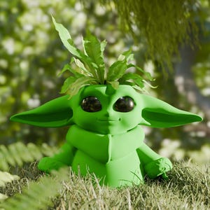 May include: A green Grogu-shaped planter with large ears and big eyes, filled with green leafy plants. The planter is sitting in a bed of grass, with a blurred green background of foliage.