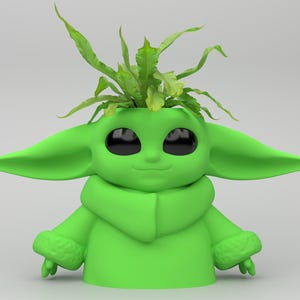 May include: A green planter shaped like a character with large ears and eyes, holding a small plant. The planter has a smooth finish and is filled with green foliage, creating a unique decorative item.