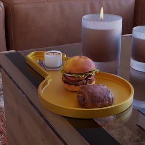 Può includere: Un vassoio giallo a forma di chitarra contiene una tazzina di caffè con un cucchiaino, un hamburger e un croissant al cioccolato. Una candela accesa e un bicchiere sono sullo sfondo. Il vassoio è su un tavolo di vetro.