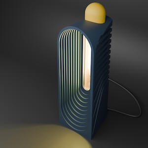 Puede incluir: Una lámpara de mesa moderna, azul marino, con una parte superior redondeada amarilla. La lámpara tiene un diseño vertical y rectangular con una serie de líneas verticales curvas en la parte delantera. Una luz cálida brilla desde el interior, y un cable gris se extiende desde la base.