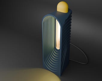 May include: A modern, navy blue table lamp with a yellow, rounded top. The lamp has a vertical, rectangular design with a series of curved, vertical lines on the front. A warm light shines from within the lamp, and a gray cord extends from the base.