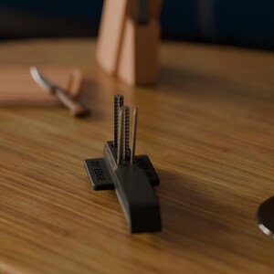 Puede incluir: Un afilador de cuchillos negro con tres varillas met&aacute;licas verticales. La base del afilador tiene el texto "35&deg; EDGE" y "SAFETY GUIDES". Un bloque de cuchillos de madera y un cuchillo est&aacute;n en el fondo.