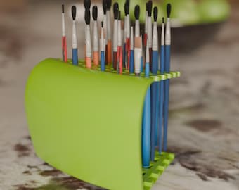 May include: A lime green paint brush holder filled with various paint brushes. The brushes have black, white, blue, orange, and red handles and bristles. The holder is made of plastic and has a curved design.
