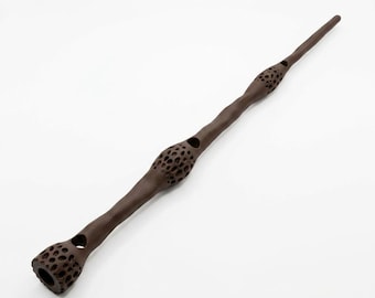 May include: A long, slender, dark brown wand featuring a textured, porous surface with numerous small, circular indentations. The design includes three distinct, bulbous sections along its length, each covered in a honeycomb-like pattern.
