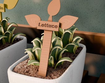 May include: A wooden garden marker with the word "Lettuce" is placed in a white planter filled with soil and green and white plants. The marker has a leaf-shaped top. The background is a speckled green wall.