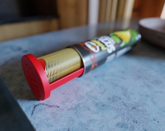 May include: A cylindrical container of potato chips with a red base and a red sliding mechanism. The chips are golden and stacked inside the container. The container has a black and silver label with the brand name and a graphic of a lime and a pepper.
