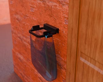 May include: A black wall-mounted holder with a clear, blue-tinted plastic bag attached. The holder is mounted on a textured orange wall next to a wooden door. The bag appears to be empty.