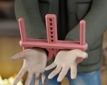 May include: A pink wooden object with a rectangular base and vertical supports. The object has a series of rectangular cutouts and is held by a person. The background is blurred, with a glimpse of a fireplace and clothing.