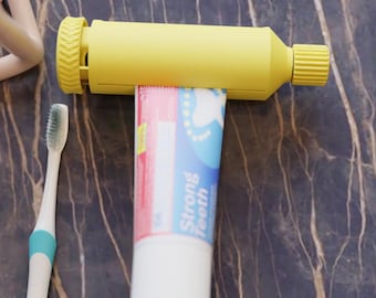 May include: A yellow toothpaste tube squeezer with a tube of toothpaste and a toothbrush. The toothpaste tube is white and red with the words "Strong Teeth" in blue. The toothbrush is white with a teal handle.