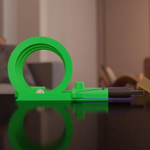 May include: A bright green, 3D-printed toy with a loop-de-loop design. A small silver ball sits at the base of the loop. A black and purple object is attached to the toy with blue string. The toy is on a dark surface.