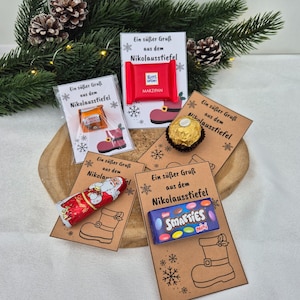 May include: Four individual gift cards featuring the text Ein süßer Gruß aus dem Nikolausstiefel and a boot illustration. The cards hold a Ritter Sport Marzipan bar, a Ferrero Rocher, a Lindt Santa figure, and a box of Smarties mini candies.
