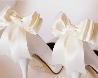 May include: A pair of white high-heeled shoes with ivory satin bows attached to the back of each shoe.