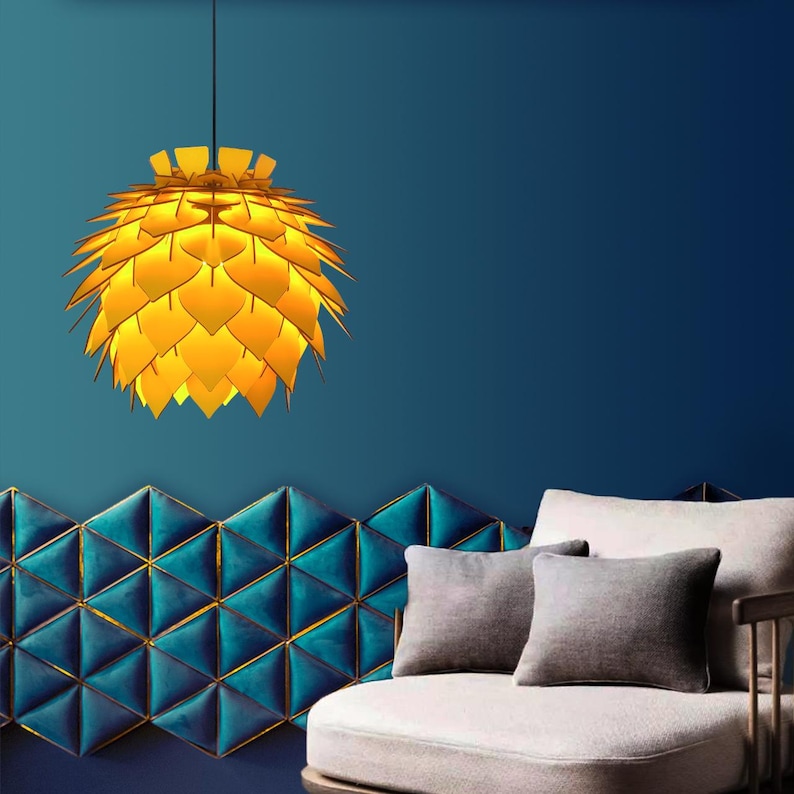 May include: A modern, yellow pendant light with a layered, petal-like design hangs from the ceiling. The light fixture is suspended against a deep blue wall, with a geometric teal and gold accent wall below. A neutral-toned sofa with gray pillows completes the scene.