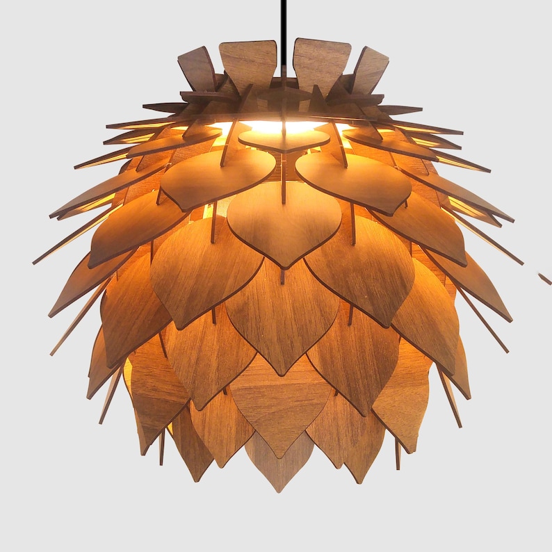 May include: A wooden pendant light fixture with a layered design. The light is made of many wooden leaf-shaped pieces, creating a unique, natural aesthetic. The fixture is suspended from a black cord and emits a warm glow.